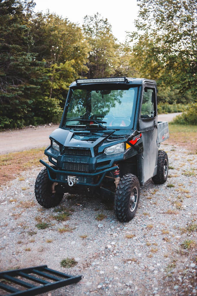 Old all terrain vehicle parked on rough walkway near ladder and bright trees under sky