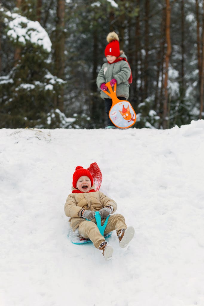 Two kids enjoying a winter day sledding in the snow, smiling and playing.