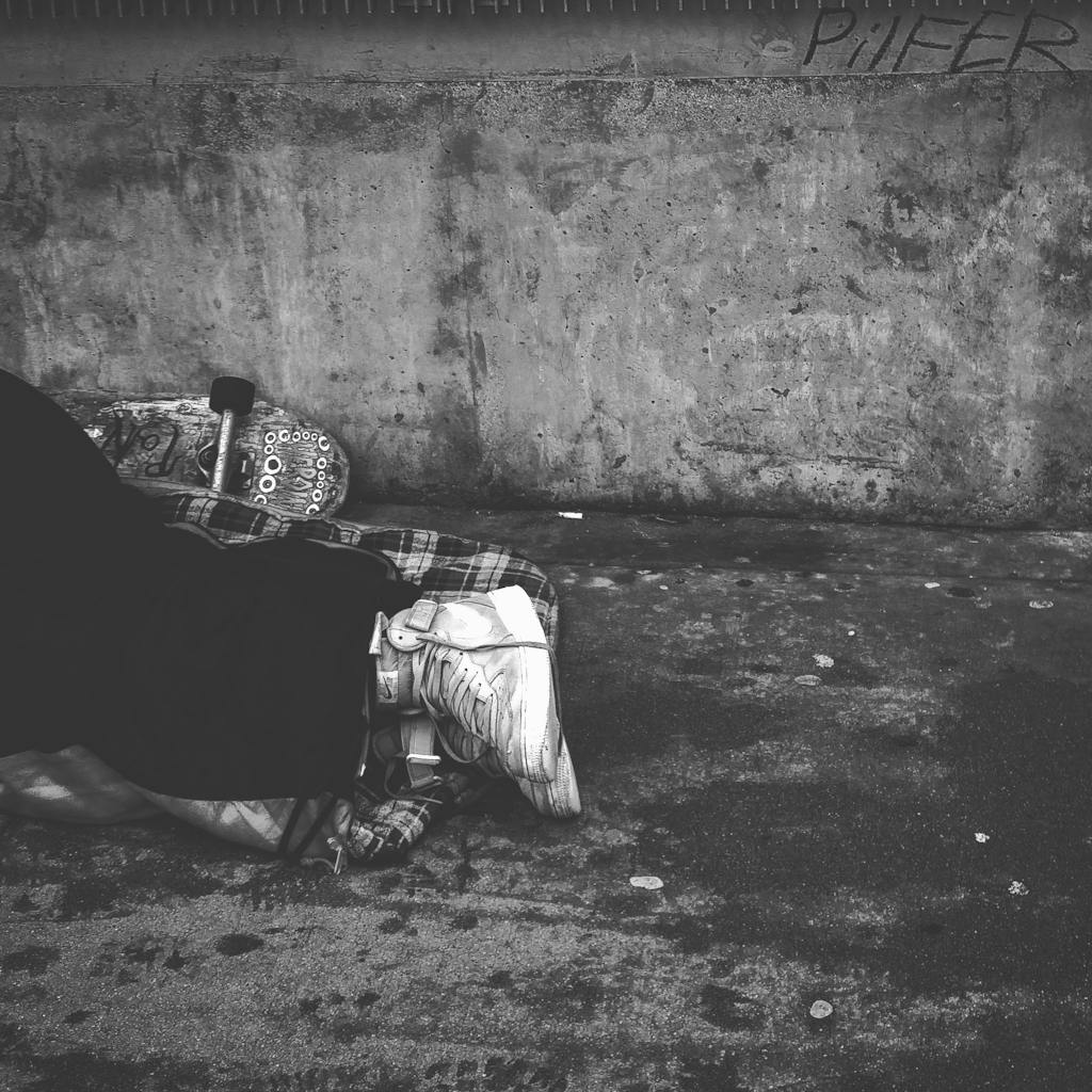 Black and white image of a person sleeping on the sidewalk, depicting urban hardship.