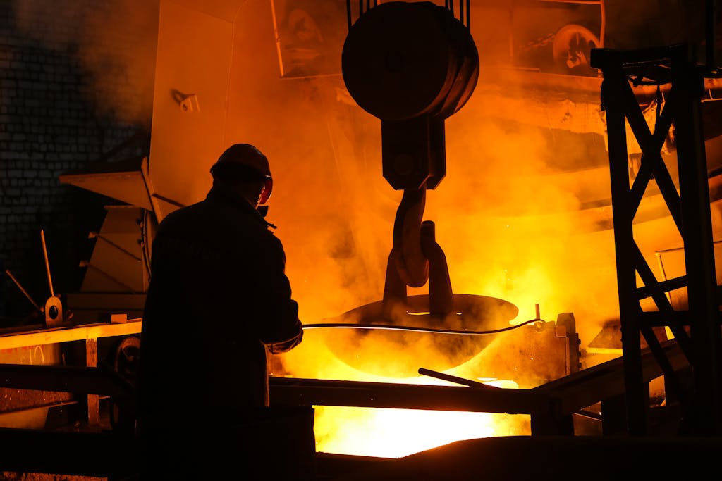 Silhouette of a worker managing molten metal in a glowing furnace, conveying industry heat and hard work.